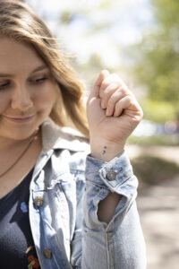 Amanda looks at her upheld wrist, showing her semicolon tattoo.