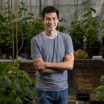 Sterling Evans stands amid a greenhouse, arms folded, smiling at the camera.