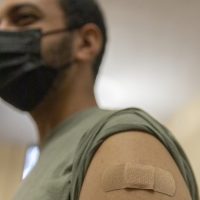 Man in a face mask wearing a bandaid on his left bicep.