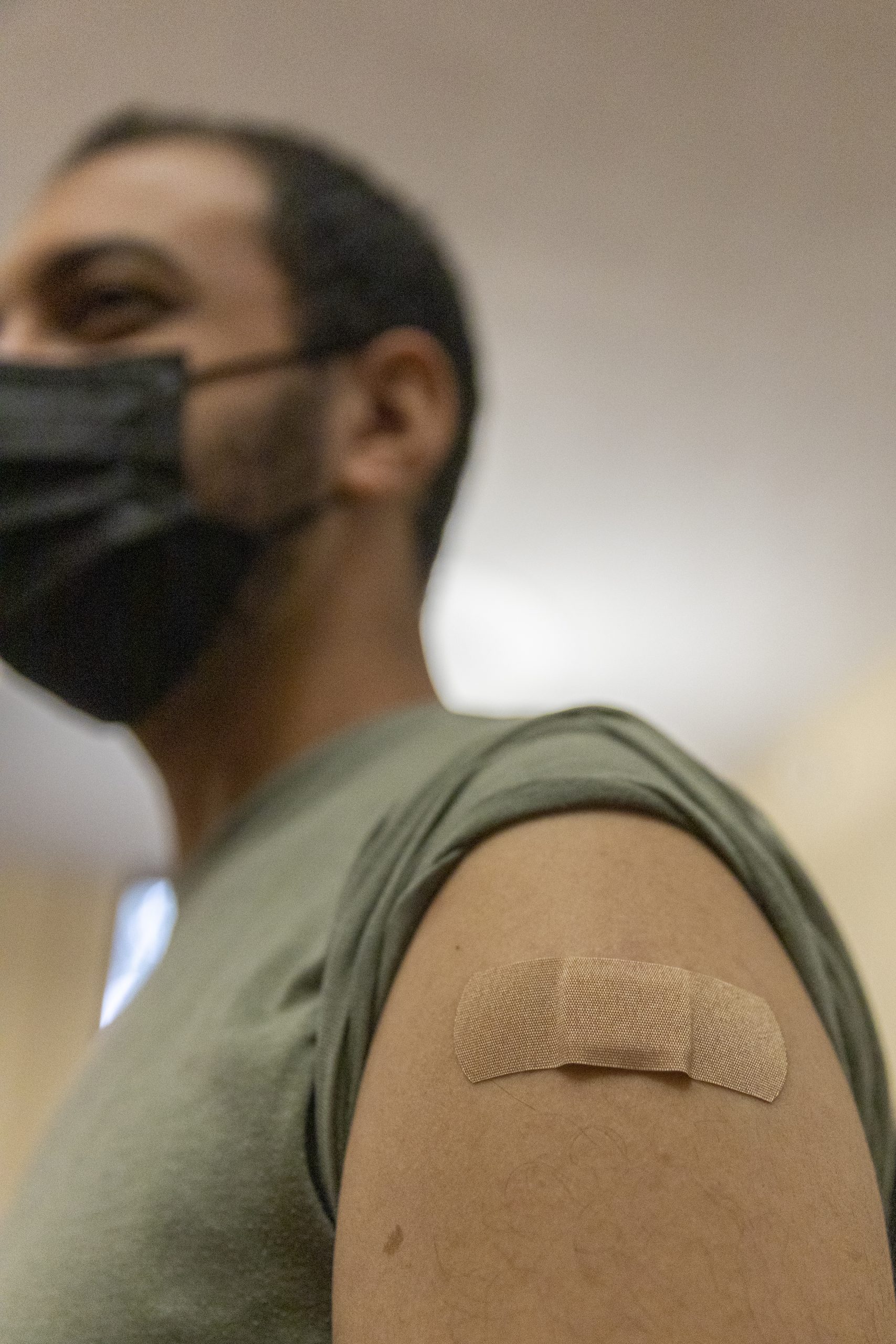 Man in a face mask wearing a bandaid on his left bicep.